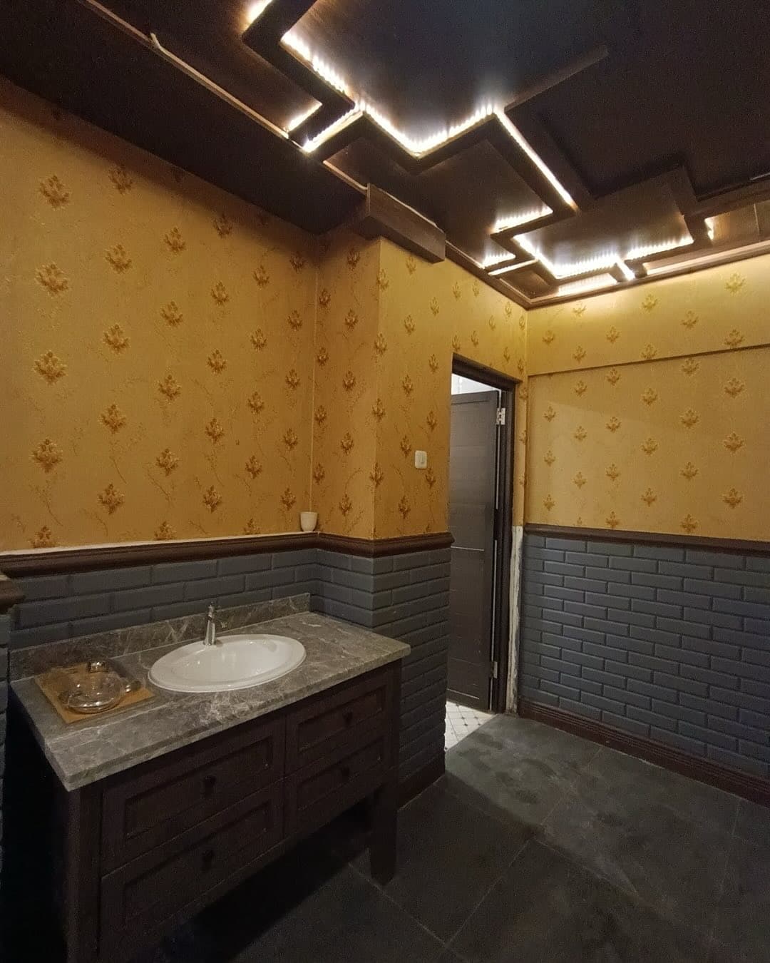 Bathroom with patterned wallpaper, dark tile wainscot, and a marble vanity
